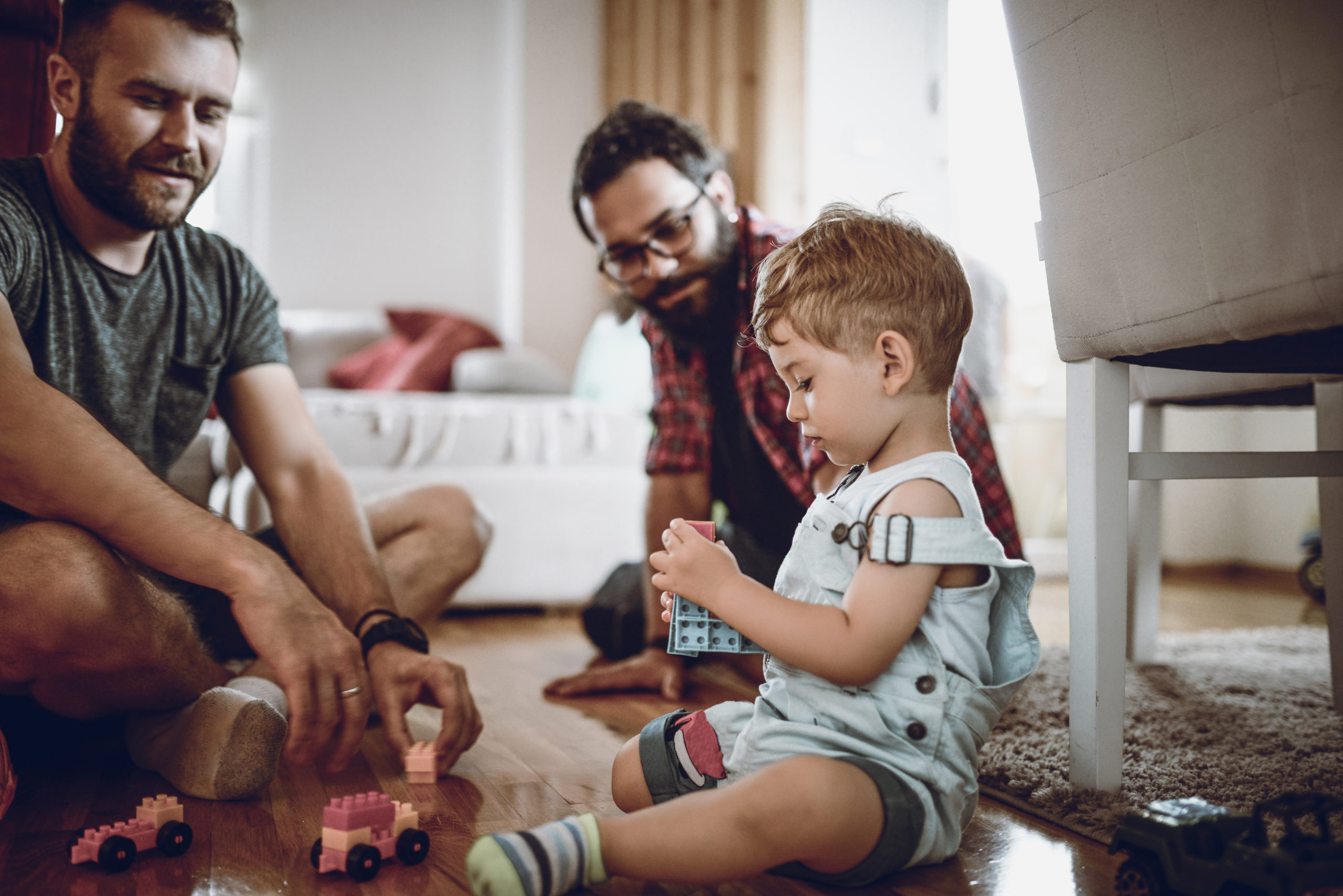 LGBTQ+ family made of two gay husbands playing with adopted baby son and his toys